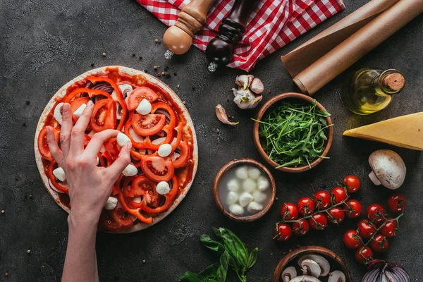 Cropped shot of woman spreading mozzarella pieces onto pizza on concrete table — Stock Photo