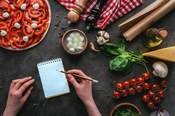 Schnappschuss von Frau, die Notizen schreibt, während sie Pizza auf Betontisch zubereitet — Stockfoto