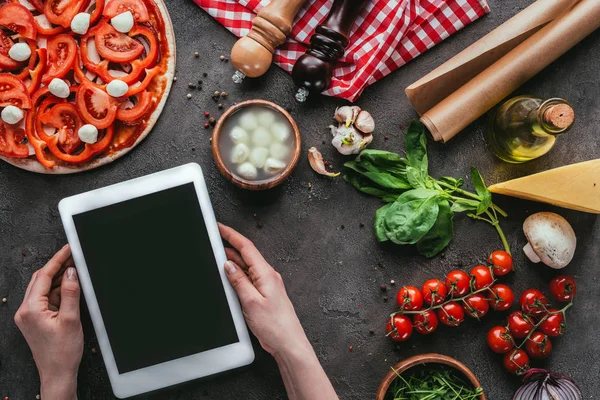 Colpo ritagliato di donna utilizzando tablet durante la preparazione di pizza sul tavolo di cemento — Foto stock