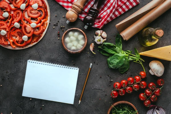 Top view of uncooked pizza with blank notebook for recipe on concrete table — Stock Photo