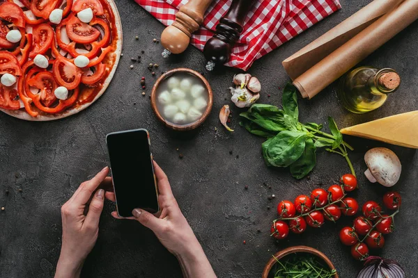 Tiro recortado de la mujer usando el teléfono inteligente mientras se prepara la pizza en la mesa de hormigón — Stock Photo
