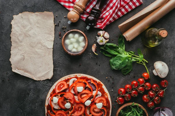 Draufsicht auf ungekochte Pizza mit Zutaten und leerem Papier auf Betontisch — Stockfoto