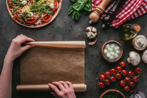 Tiro cortado de mulher com papel de pergaminho preparando pizza na mesa de concreto — Fotografia de Stock