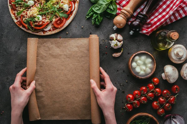Colpo ritagliato di donna con carta pergamena preparare pizza fatta in casa su tavolo di cemento — Foto stock