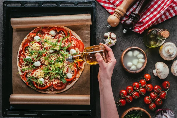 Recortado tiro de mujer vertiendo aceite sobre deliciosa pizza sobre mesa de hormigón - foto de stock