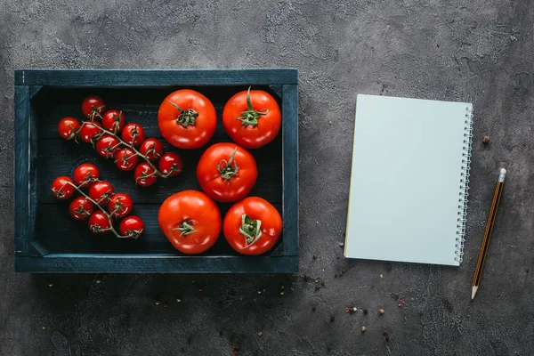 Top view of tomatoes in box and notebook on concrete surface — Stock Photo