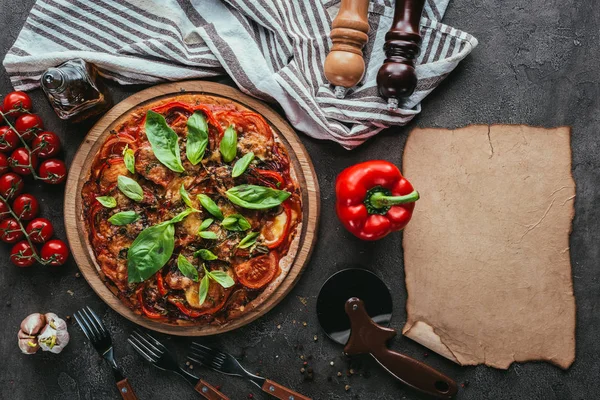 Vista superior de la pizza recién horneada con ingredientes y papel en blanco en la mesa de hormigón - foto de stock