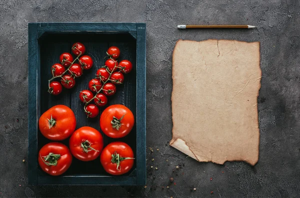 Top view of tomatoes in box and blank paper on concrete surface — Stock Photo
