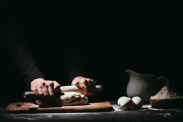 Cropped shot of person preparing dough with rolling pin on black — Stock Photo