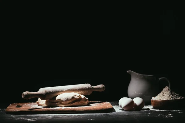 Dough with ingredients and rolling pin on black — Stock Photo