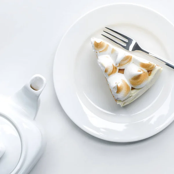 Vista superior de delicioso pedazo de pastel con merengue y tetera en la mesa blanca - foto de stock