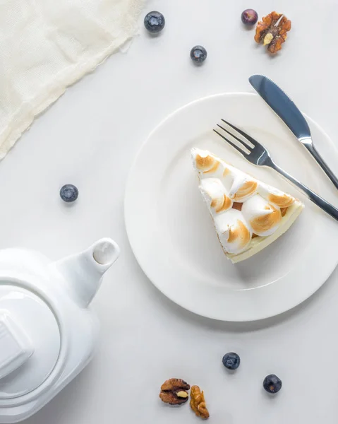 Vue de dessus du morceau appétissant de gâteau avec meringue et théière sur table blanche — Photo de stock