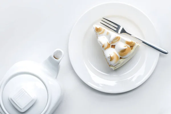Верхний вид чайник и вкусный кусок торта с безе на белом столе — стоковое фото