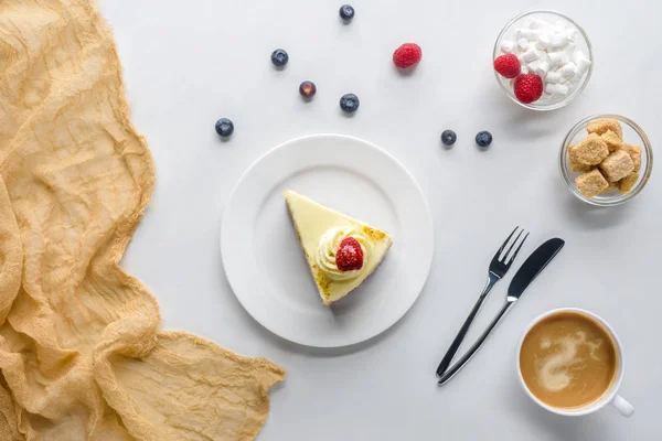 Vista dall'alto di un pezzo di torta con bacche e caffè su un tavolo bianco — Foto stock