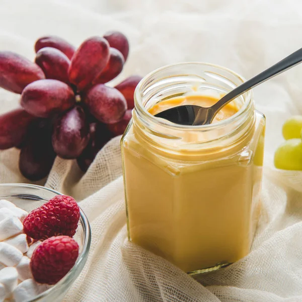 Appetizing jar of honey with grapes on tablecloth — Stock Photo
