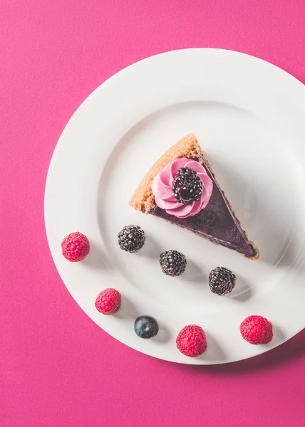 Vista superior de pedaço apetitoso de bolo com bagas na placa na superfície rosa — Fotografia de Stock