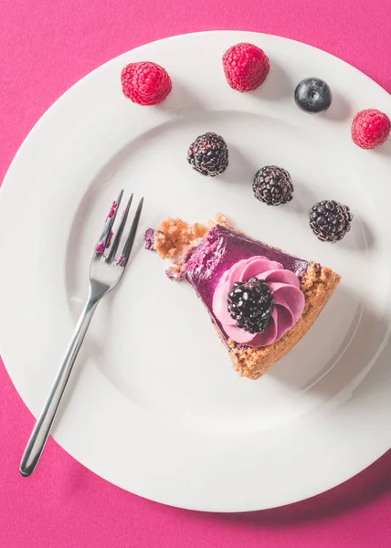 Vista dall'alto di pezzo di torta morso con bacche sul piatto sulla superficie rosa — Foto stock