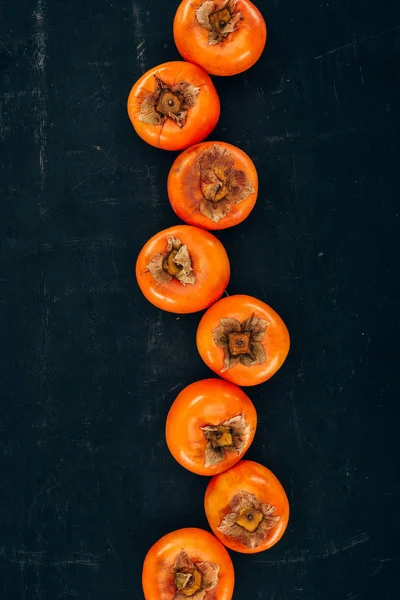 Top view of row of persimmons on black — Stock Photo