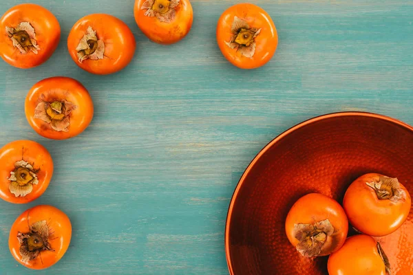 Top view of persimmons on red plate and turquoise table — Stock Photo