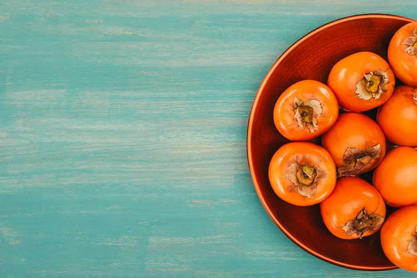 Top view of persimmons on red plate on turquoise table — Stock Photo