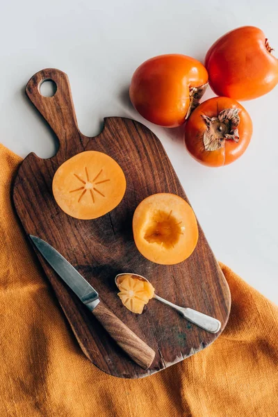 Top view of persimmons on wooden board with knife and spoon — Stock Photo