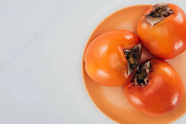 Top view of persimmons on orange plate isolated on white — Stock Photo