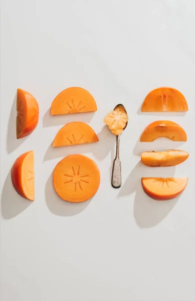 Top view of persimmons pieces and spoon on white — Stock Photo