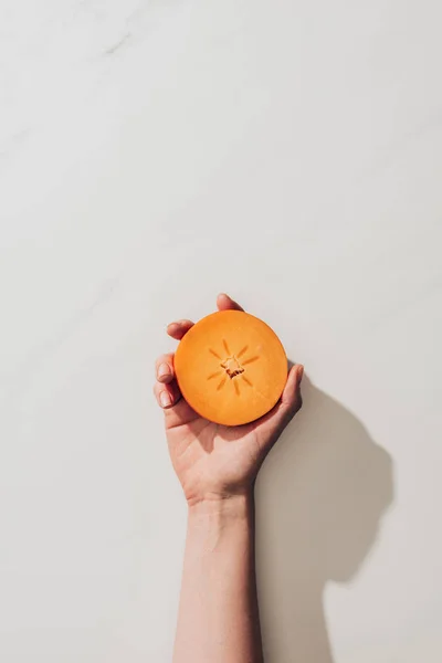 Cropped image of woman holding persimmon piece in hand on white — Stock Photo