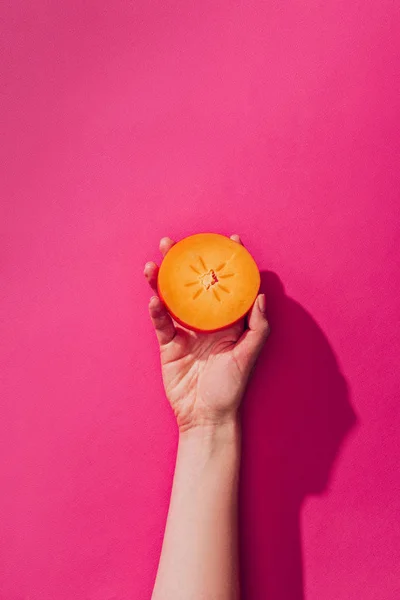 Elevated view of woman holding persimmon piece on pink — Stock Photo