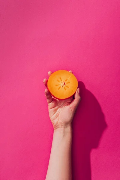 Erhabene Ansicht einer Frau mit Persimmon-Stück auf rosa — Stockfoto