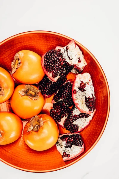 Elevated view of persimmons and pomegranates on red plate isolated on white — Stock Photo