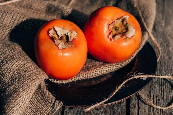 Dois deliciosos cáqui em pano de saco na mesa de madeira — Fotografia de Stock