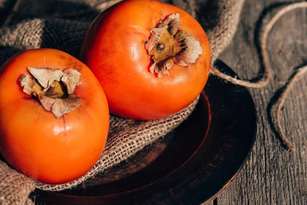 Deux kaki mûrs sur un sac sur une table en bois — Photo de stock