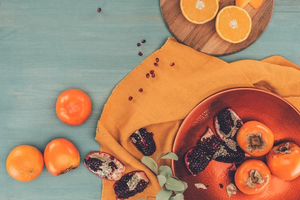 Draufsicht auf Kaki mit Orangen und Granatäpfeln auf türkisfarbenem Tisch — Stockfoto