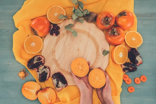 Cropped image of woman holding two pieces of persimmon — Stock Photo