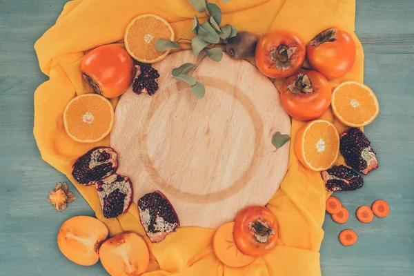 Holzteller von oben zwischen Kaki mit Orangen und Granatäpfeln — Stockfoto