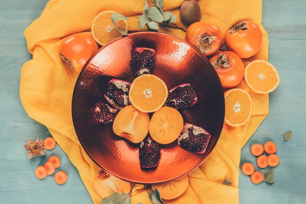 Top view of persimmons with oranges and pomegranates on plate on orange tablecloth — Stock Photo