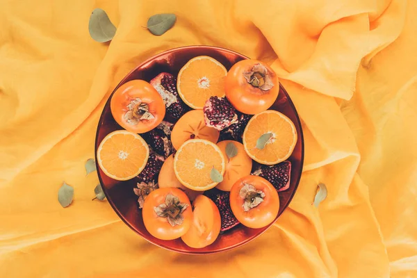 Вид сверху на фрукты на тарелке на апельсиновой скатерти — стоковое фото
