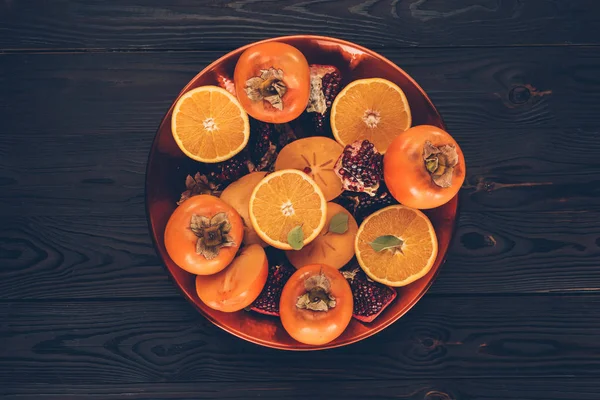 Kaki mit geschnittenen Orangen und Granatäpfeln auf dem Teller auf dem Tisch — Stockfoto