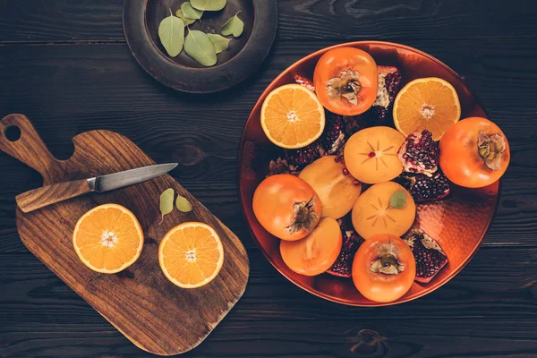 Top view of persimmons with cut oranges and pomegranates on plates and wooden board — Stock Photo