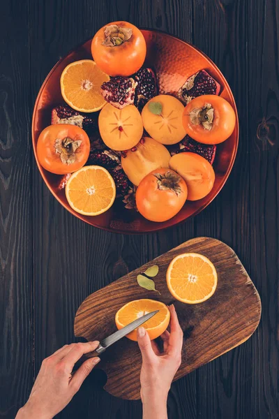 Image recadrée de la femme coupant orange sur panneau en bois — Photo de stock