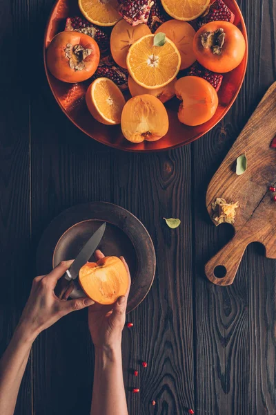 Image recadrée de femme coupant persimmon — Photo de stock