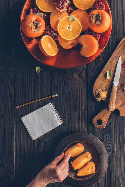 Abgeschnittenes Bild einer Frau, die ein Stück Persimmon nimmt — Stockfoto