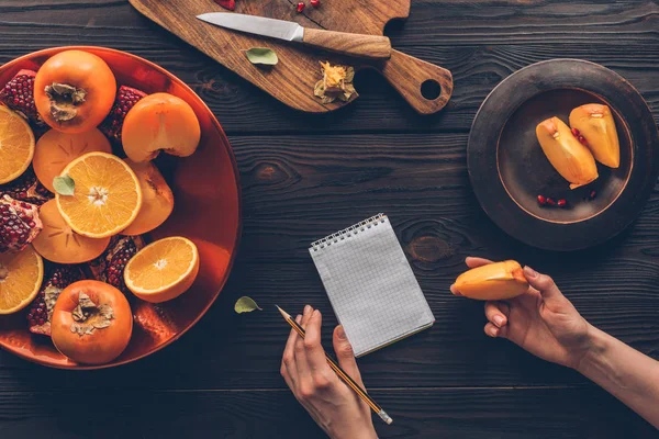 Cropped image of woman holding pencil and persimmon piece — Stock Photo