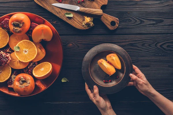 Cropped image of woman holding plate with persimmon pieces — Stock Photo