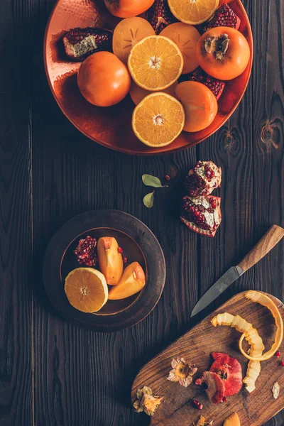 Vista elevada de caquis con naranjas y granadas en placas - foto de stock