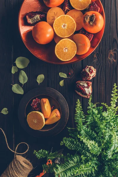 Vue de dessus des kaki avec des oranges coupées et des grenades sur des assiettes sur une table en bois — Photo de stock