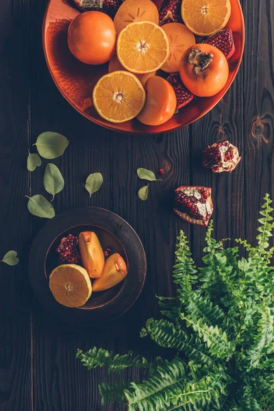 Top view of persimmons with cut oranges and pomegranates on plates — Stock Photo