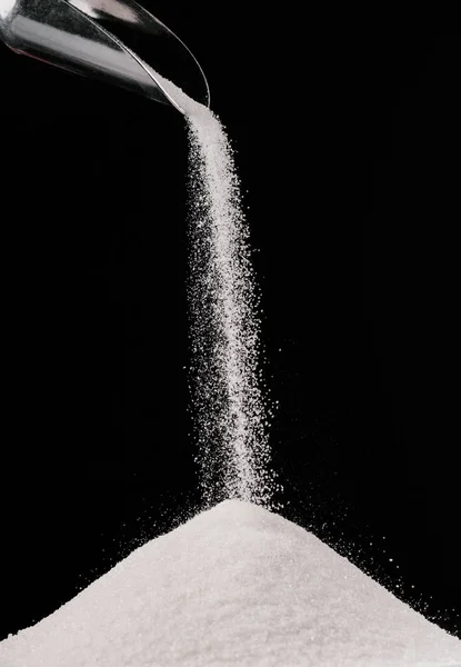 Açúcar caindo de colher de metal na pilha isolada em preto — Fotografia de Stock