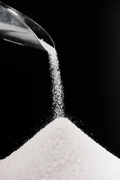 White sugar falling from metal scoop on pile isolated on black — Stock Photo